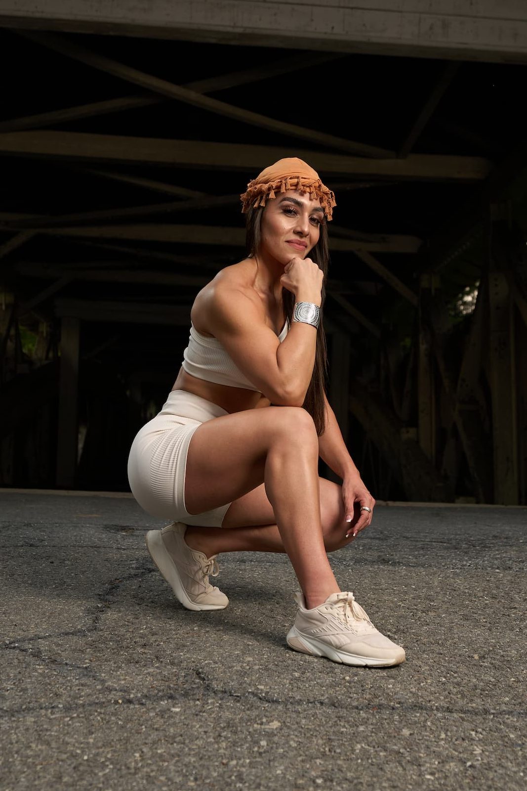 Gera squatting with confidence under a bridge, smiling and grounded — embodying strength, authenticity, and feminine power.